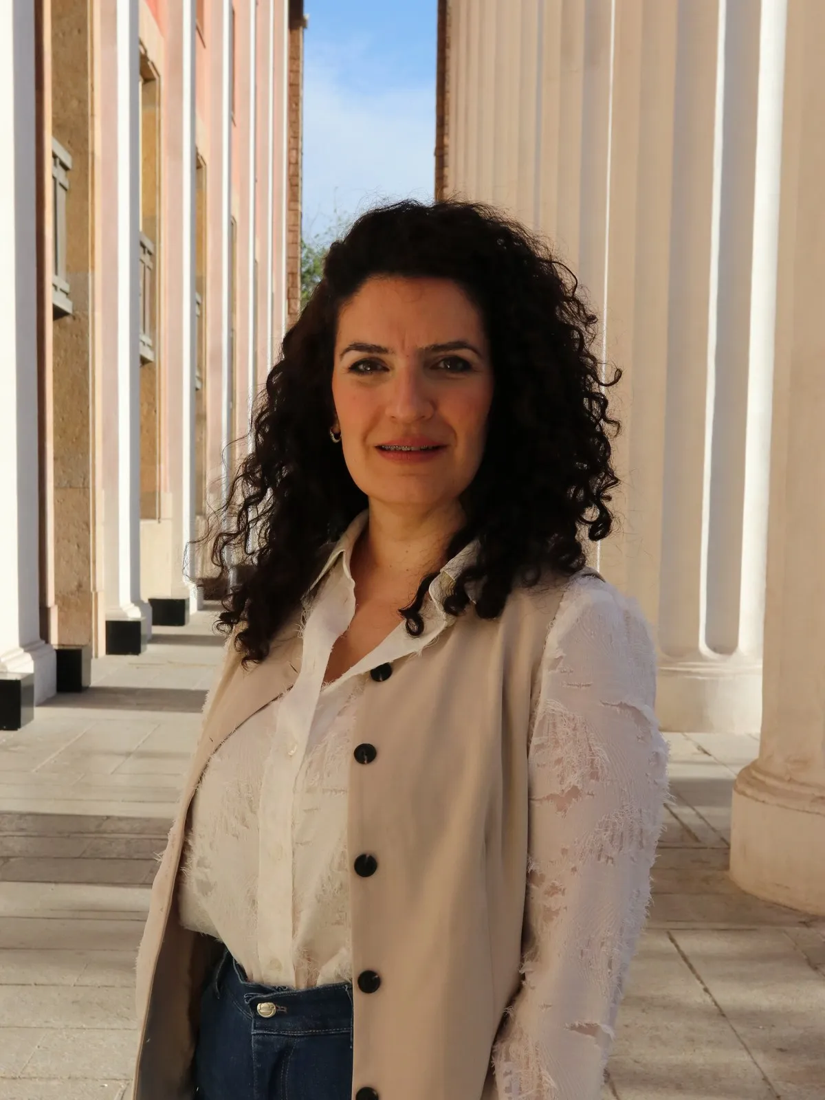 Retrato de María Cecilia Granzini, de chaleco beige y camisa blanca, frente a una columnata