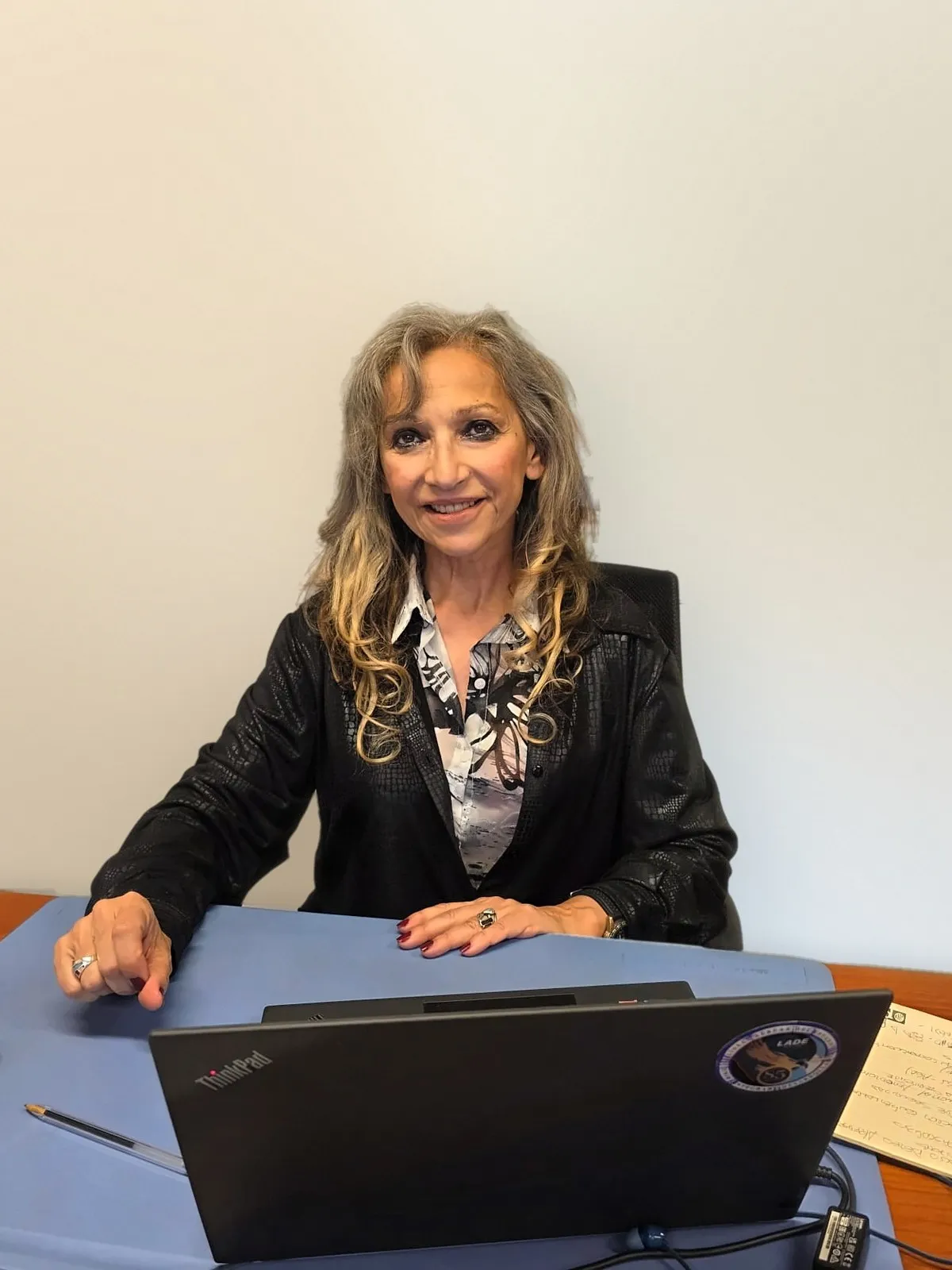 Myriam Gea sonriente en su escritorio, con saco negro, frente a una computadora portátil